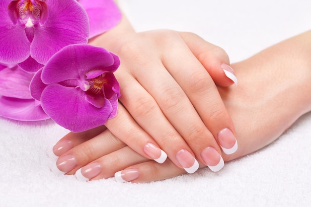 Kobiece dłonie z french manicure z fioletowymi kwiatami orchidei