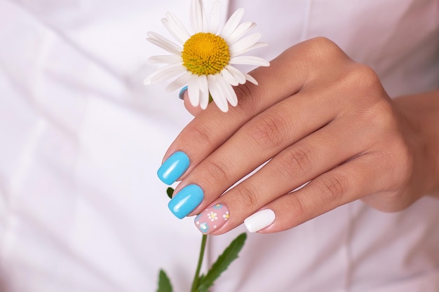 Kobiece dłonie z letnimi paznokciami do manicure, ozdobione kwiatami rumianku