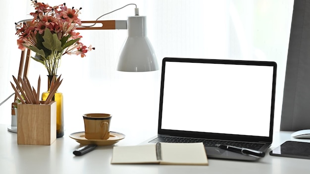 Kobiece miejsce pracy z laptopem, filiżanką herbaty i doniczką na białym stole