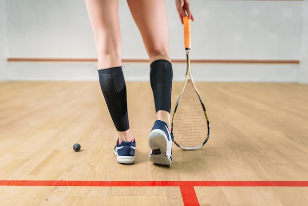Kobiece nogi gracza w squasha, rakieta i piłka, kryty klub treningowy