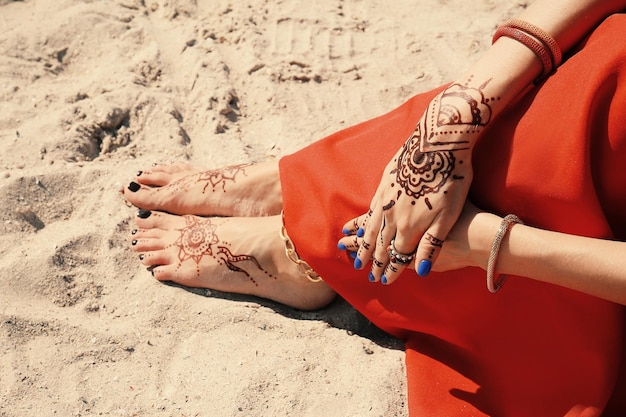 Kobiece nogi i ręce z tatuażem z henny na tle piasku na plaży