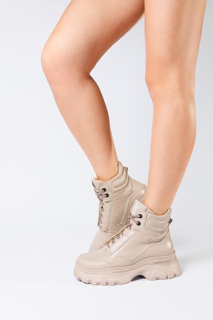 Kobiece nogi w beżowych skórzanych butach z nowej kolekcji na białym tle damskie nogi w modnych butach z ekoskóry wiosna 2022