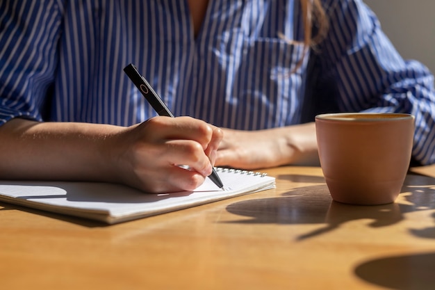 Kobiece pisanie notatek plany w notatniku na drewnianym stole z filiżanką kawy kobiety ręce w drewnie