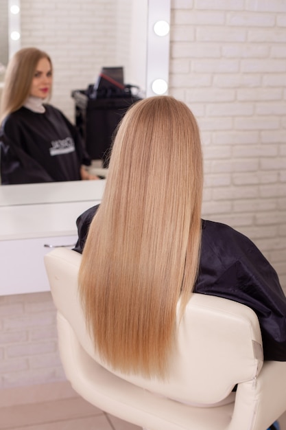 Kobiece plecy z długimi prostymi blond włosami w salonie fryzjerskim
