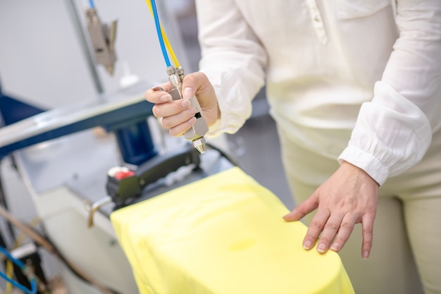 Kobiece ręce czyszczące plamę z żółtych ubrań przy użyciu specjalnego urządzenia w pralni chemicznej, twarz nie jest widoczna