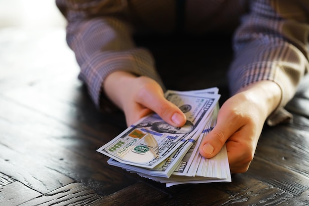 Kobiece ręce liczące amerykańskie banknoty stu dolarowe na tle mniejszych banknotów leżących na stole