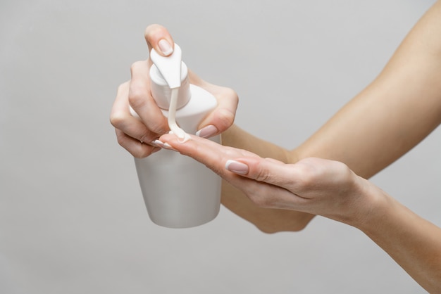 Kobiece ręce przy użyciu żelu do dezynfekcji rąk lub dozownika mydła w płynie na jasnoszarej ścianie