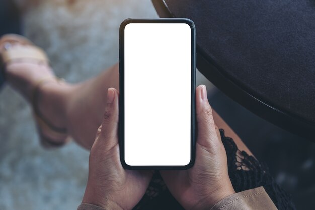 Kobiece ręce trzymając czarny telefon komórkowy z pustym białym ekranem siedząc w kawiarni
