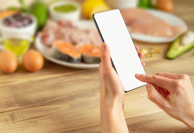 Kobiece ręce trzymając smartfon z pustym ekranem nad jedzeniem w tle koncepcja zamówienia online