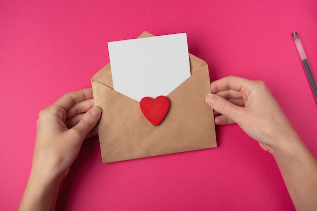 Kobiece ręce trzymające kopertę rzemieślniczą z pustym arkuszem i czerwonym sercem. Koncepcja Walentynki.