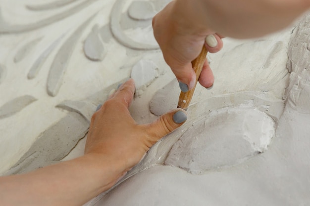 Kobiece ręce w pracy rzeźbią płaskorzeźbę za pomocą instrumentu