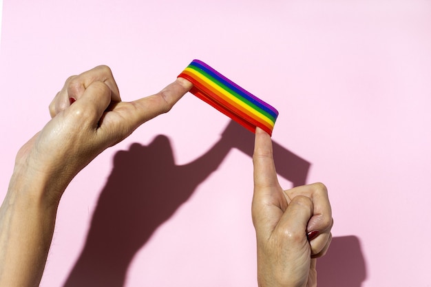 Kobiece ręce z bransoletką LGBT na różowym tle