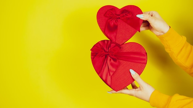 Kobiece ręce z czerwonymi pudełkami prezentowymi w formie serca na żółtym tle Nie do poznania osoba trzymająca romantyczne prezenty ze wstążką Koncepcja prezentu na walentynki i międzynarodowy dzień kobiet