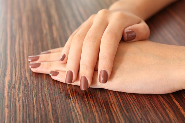 Zdjęcie kobiece ręki z brązowym manicure'em na drewnianym tle