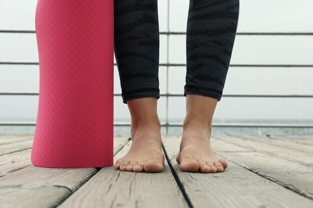 Zdjęcie kobiece stopy i różowa matka do jogi na drewnianej podłodze na zewnątrz
