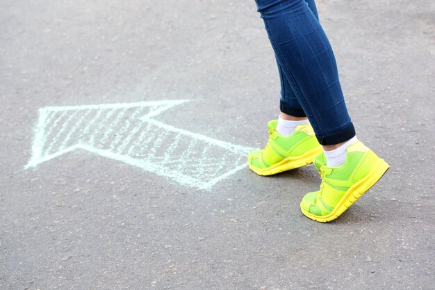 Zdjęcie kobiece stopy i rysowanie strzały na tle chodnika