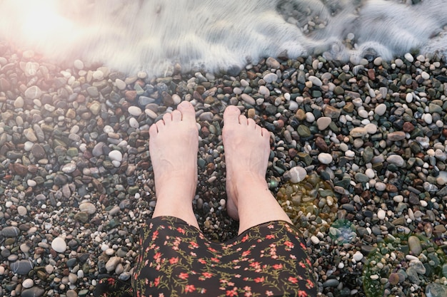 Kobiece stopy nad wodą na kamienistej plaży