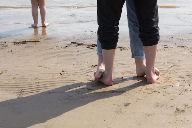 Kobiece stopy stojące na stopach mężczyzny i stopy dziecka na piaszczystej plaży boso
