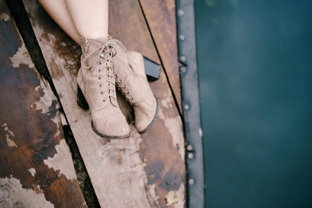 Kobiece stopy w butach na wysokim obcasie na drewnianym molo nad zbliżeniem wody