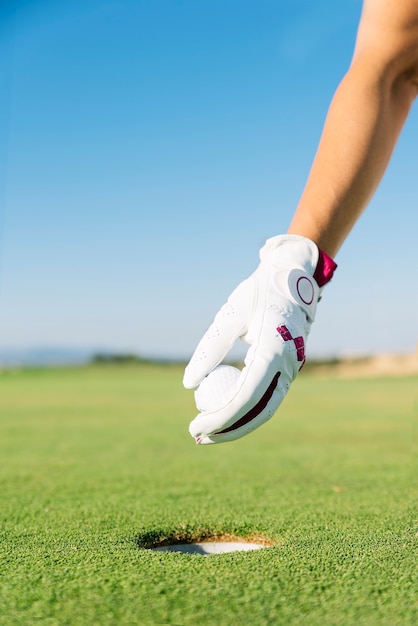 Kobiecej ręki wprowadzenie piłki golfowej do dołka na zielonym polu. Koncepcja golfa.