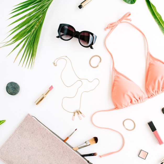 Kobiecy letni strój kąpielowy bikini i akcesoria kolaż na białym tle z gałązkami palmowymi, naszyjnikiem i okularami przeciwsłonecznymi.