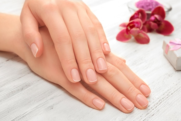 Kobiet ręki z pięknym manicure'em i purpurową orchideą na drewnianym tła zakończeniu up