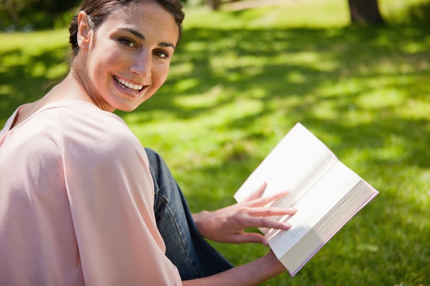 Kobiet spojrzenia jej strona podczas gdy czytający książkę w trawie