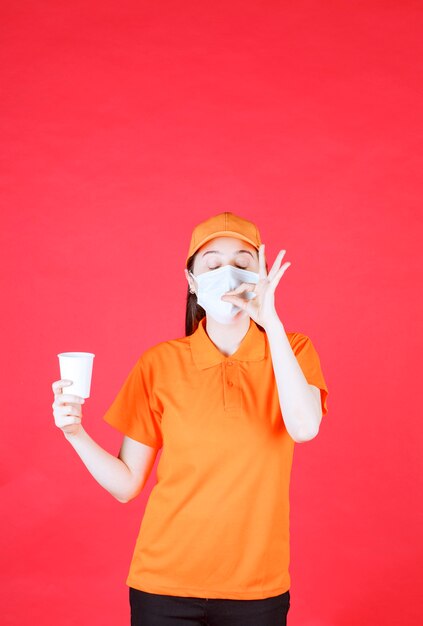 Kobieta Agentka W Kolorze Pomarańczowym Dresscode I Maska, Trzymająca Jednorazowy Kubek I Pokazująca Pozytywny Znak Ręki.