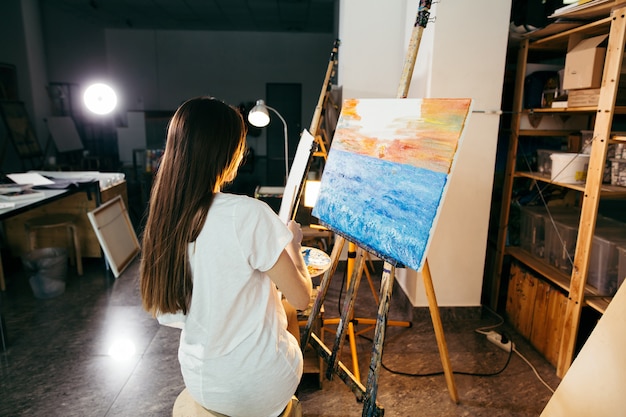 Kobieta artysta malujący obraz na sztalugach farbami olejnymi w swoim warsztacie