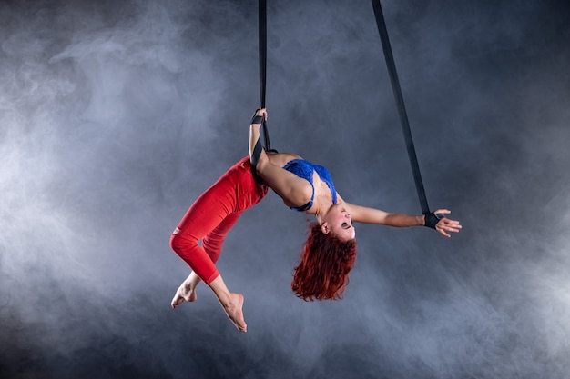 Kobieta atletyczna, seksowna i elastyczna artystka cyrkowa antenowa z rudą na pasach antenowych na czarnym tle.