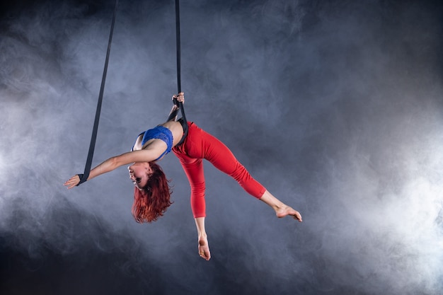 Kobieta atletyczna, seksowna i elastyczna artystka cyrkowa powietrzna z rudowłosą na paskach antenowych na czarno.