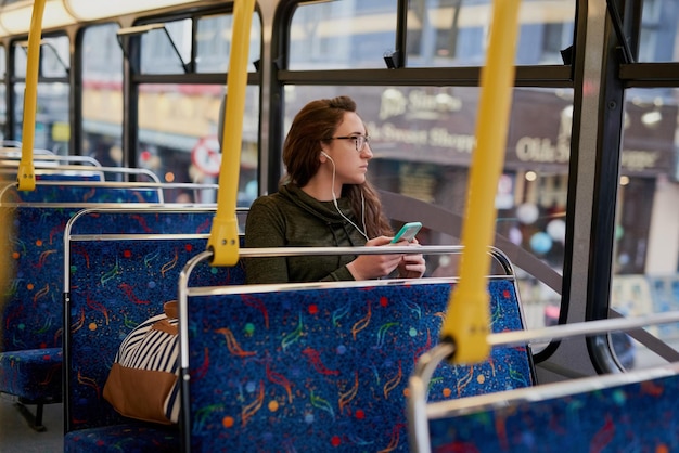 Kobieta autobus i słuchawki z telefonem do transportu podróżnego i czytania powiadomienia w sieci Osoba muzyka i smartfon z słuchaniem strumienia audio subskrypcja na aplikacji mobilnej do dojazdu