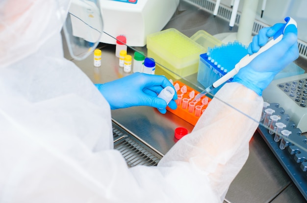 Kobieta badaczka laboratoryjna PCR w ochronnym kombinezonie medycznym z dozownikiem w rękach przeprowadza eksperyment naukowy lub opracowuje szczepionkę.
