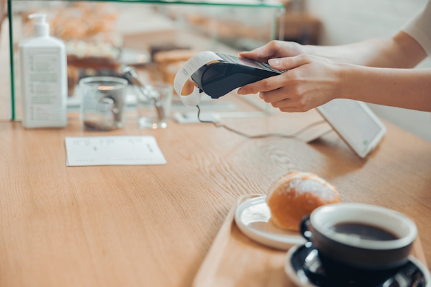 Kobieta barista korzystająca z terminala do płatności zbliżeniowych w kawiarni