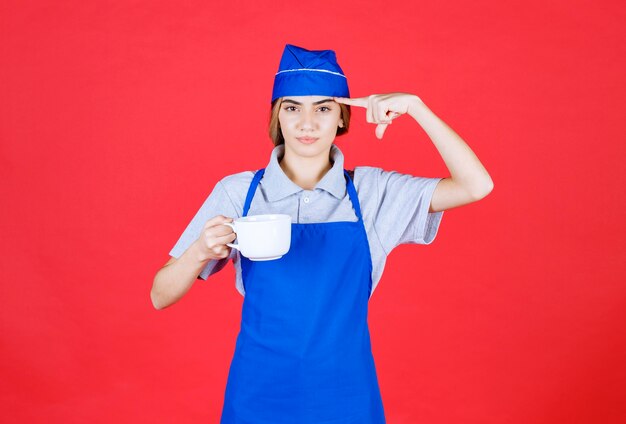 Kobieta barista trzymająca biały duży kubek i myśląca