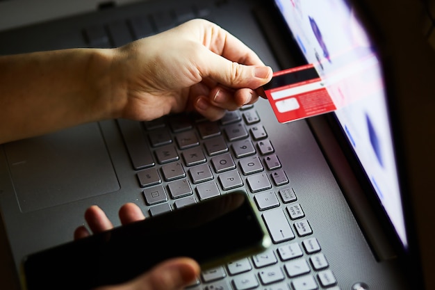 Kobieta bez twarzy wkłada kartę kredytową do laptopa. Humorystyczna koncepcja zakupów online i e-commerce