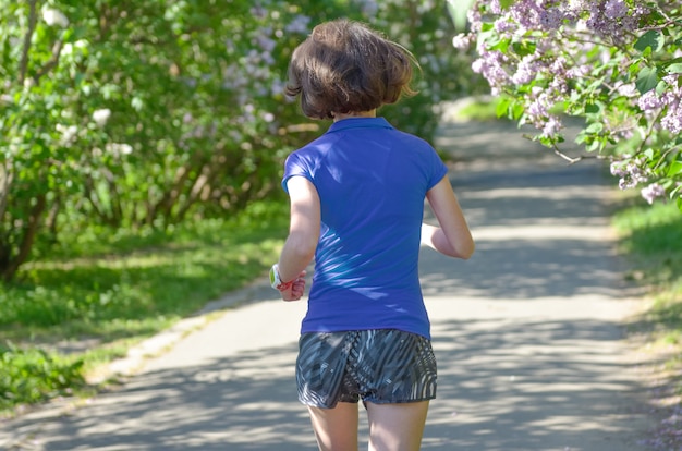 Kobieta biegacz jogging w wiosna parku z lilym okwitnięciem, rankiem biega outdoors, sprawności fizycznej i biega zdrowego stylu życia pojęcie