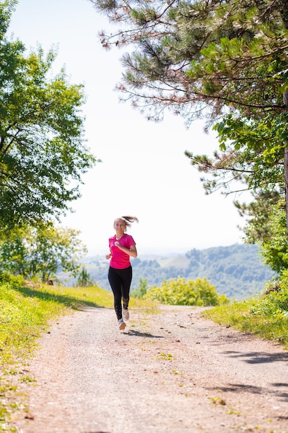 kobieta biegająca po wiejskiej drodze przez piękny słoneczny las, koncepcja ćwiczeń i fitness