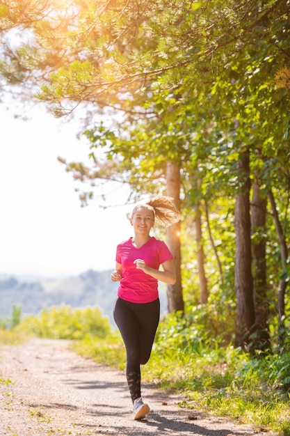 kobieta biegająca po wiejskiej drodze przez piękny słoneczny las, koncepcja ćwiczeń i fitness