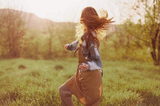 Kobieta biegnąca przez pole w letni dzień z długimi włosami w promieniach zachodzącego słońca Koncepcja wolności i harmonii z naturą