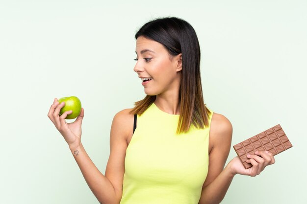 Kobieta bierze czekoladową pastylkę w jednej ręce i jabłko w drugiej