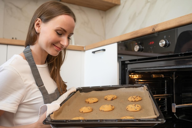 Zdjęcie kobieta bierze tacę świeżych ciasteczek z piekarnika w domu w kuchni
