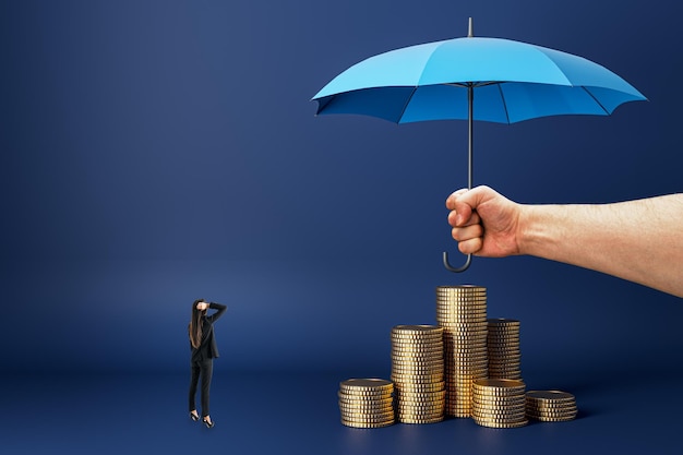 Kobieta biznesmena patrząca na abstrakcyjną rękę mężczyzny trzymającą parasol nad ułożonymi monetami na ciemno niebieskim tle Koncepcja ubezpieczeń i inwestycji