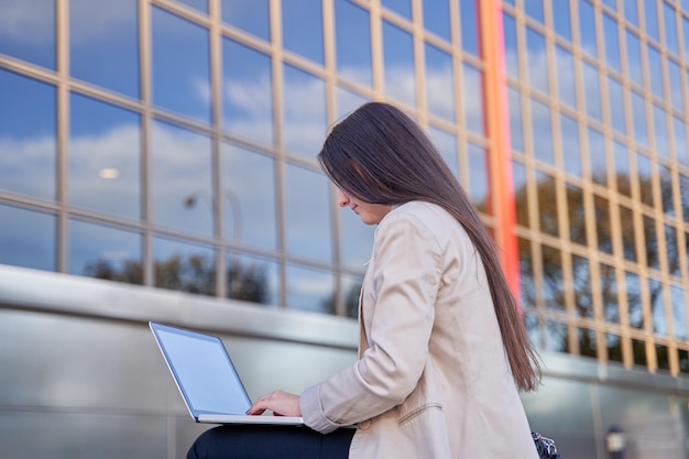 Kobieta biznesu siedzi na zewnątrz biurowca pracującego z komputerem typu laptop biznes koncepcja kopiowania miejsca na tekst