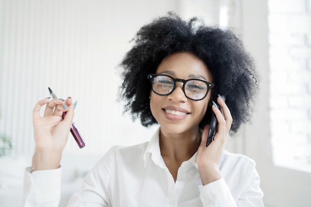 Kobieta biznesu w biurze w okularach rozmawia przez telefon, uśmiechając się i pokazując zęby