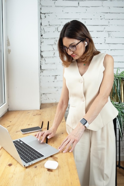 Kobieta biznesu w swoim biurze stoi przed oknem, na parapecie jest laptop Portret kobiety biznesu z rudymi włosami do ramion Kobieta patrząca na ekran laptopa