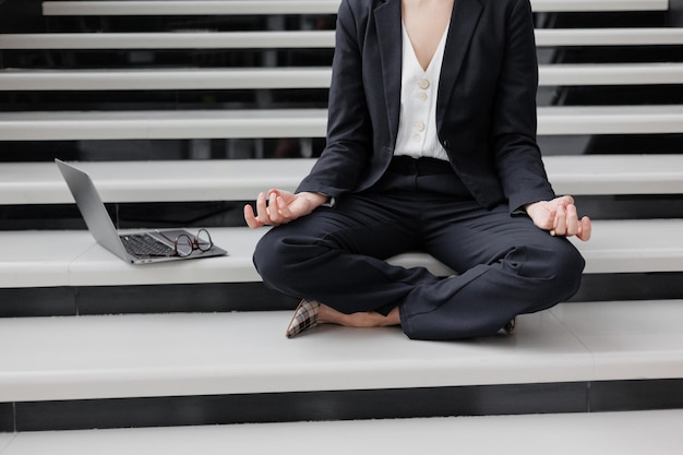 Kobieta biznesu z laptopem w biurze centrum biznesowego siedzi na schodach w pozycji lotosu i medytuje relaks