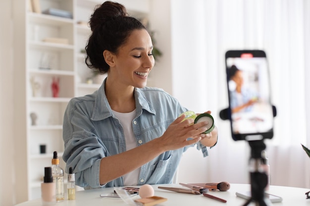 Kobieta blogerka pokazująca produkt do pielęgnacji skóry na telefon komórkowy, tworząc wideo w pomieszczeniach