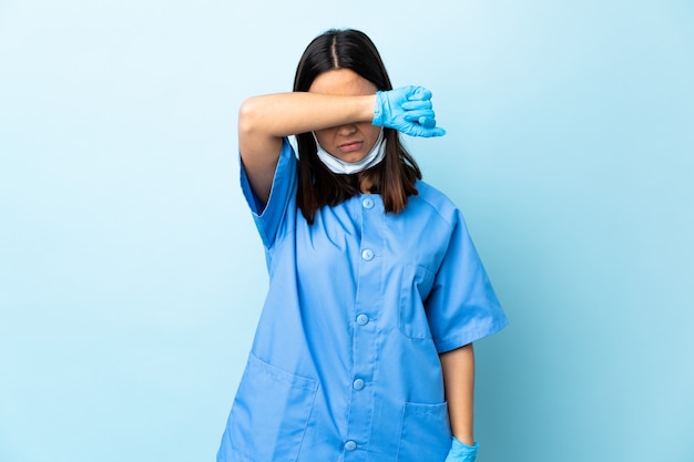Kobieta chirurg na pojedyncze niebieskie ściany obejmujące oczy rękami