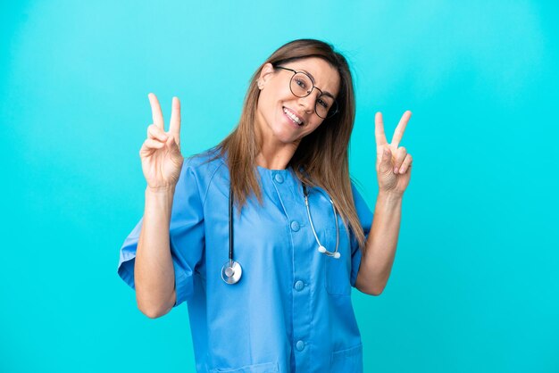 Kobieta chirurg w średnim wieku na białym tle na niebieskim tle pokazując znak zwycięstwa obiema rękami